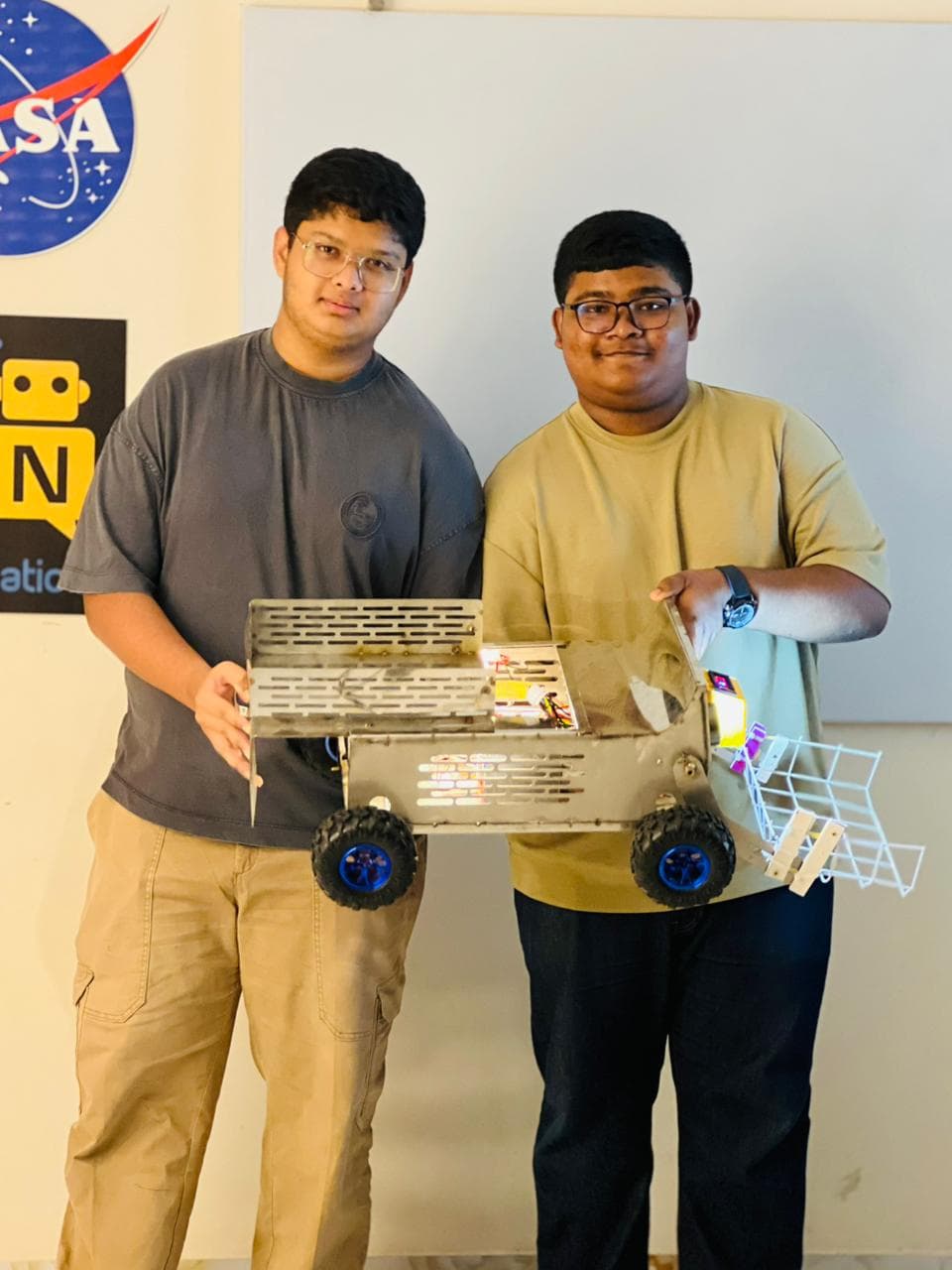 The two members of Team Paradox standing side by side, holding the stainless-steel cleaning rover between them